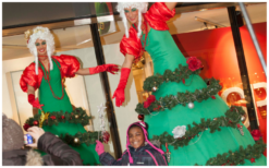 Betoverend kerstentertainment: Kerstboom Lady's Steltenlopers brengen magie met guirlandes en lampjes. Boek nu voor feestelijke sfeer!