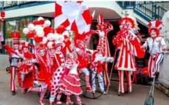 Rood wit steltenlopers duo met bellen tijdens vrolijke steltenlopers act op festival of evenement.