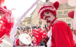 Clown op rood witte driewieler met drumstel tijdens circus thema mobiele act op festival of evenement.