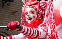 Clown op rood witte driewieler met drumstel tijdens circus thema mobiele act op festival of evenement.