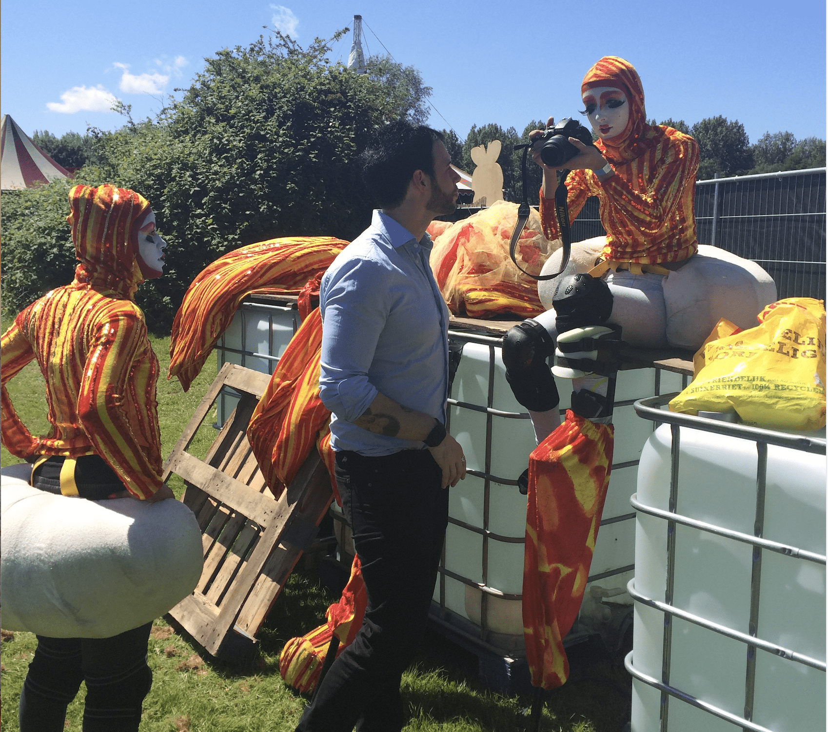 Steltenlopers maken zich gereed om op te treden in Vrolijk & Fleurig, een van onze meest vrolijke zomerse acts op stelten. Buiten op het festival is er voldoende ruimte om heerlijk in het zonnetje de kostuums aan te doen.