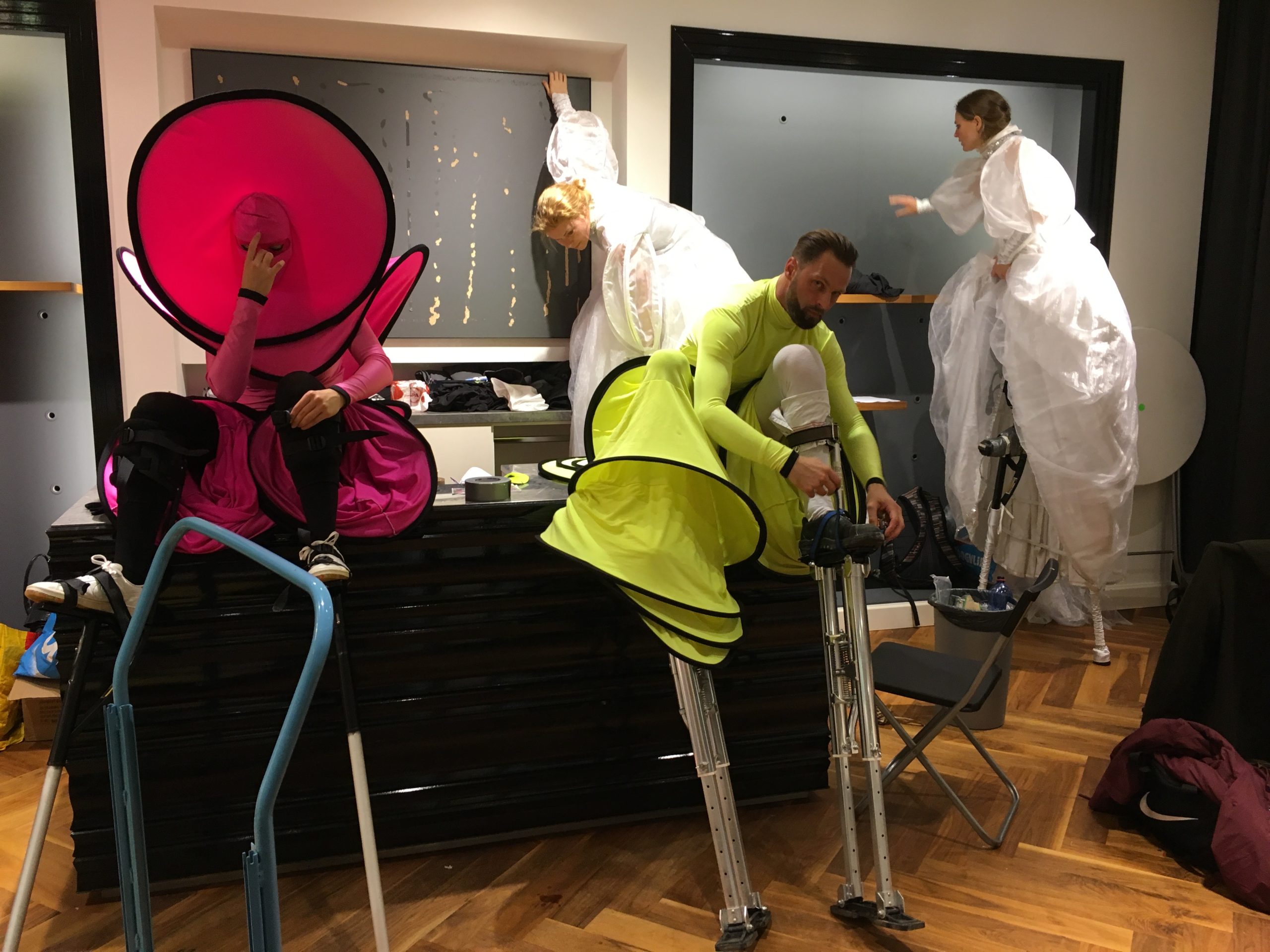 Backstage zie je hoe de steltenlopers moeilijke posities aannemen om hun stelten aan te kunnen doen. Niet altijd is de toegewezen ruimte even handig, maar door hun ervaring lukt het ze altijd om zich klaar te maken voor het optreden