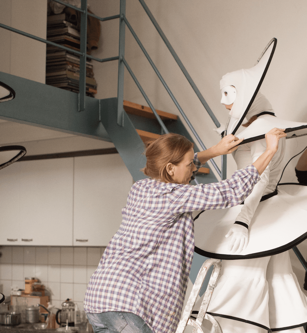 Tijdens een fotoshoot van de steltenact Circle Mania LED staat Cynthia de ingewikkelde hoofdstukken aan te doen bij een van onze top steltenlopers. Dit moment van nauwkeurige voorbereiding en samenwerking illustreert de toewijding van ons team om elk detail van onze acts perfect te maken.