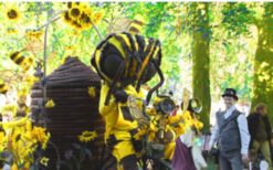 Grote bijen kostuums en dansende bijen tijdens een vrolijke Bijen Parade met duurzame fiets en zwevende bijtjes op een festival of evenement.