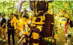 Grote bijen kostuums en dansende bijen tijdens een vrolijke Bijen Parade met duurzame fiets en zwevende bijtjes op een festival of evenement.